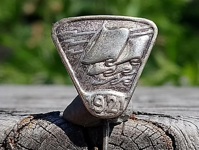 Hopeavärinen merkki vuodelta 1921. Halkaisija - 17 mm.