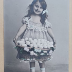 Tyttö kantaa munakoria hymyillen, vanha Pääsiäispk, p. 1906 - pikkukuva 1