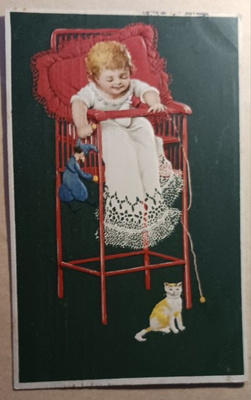 Lapsi syöttötuolissa riiputtaa nukkea, leikittää kissaa 1906